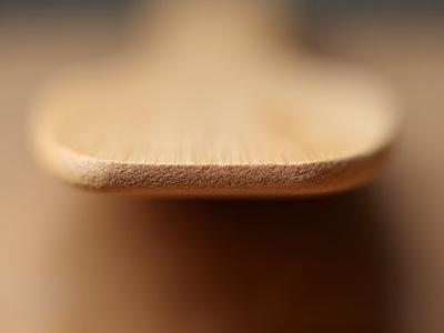 A macro shot of a wooden spatula's blade edge, showing its thin, rounded profile.